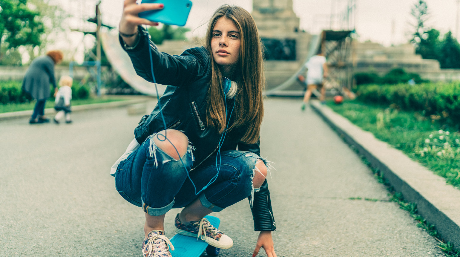 Eine Jugendliche macht ein Selfie auf dem Skateboard.  