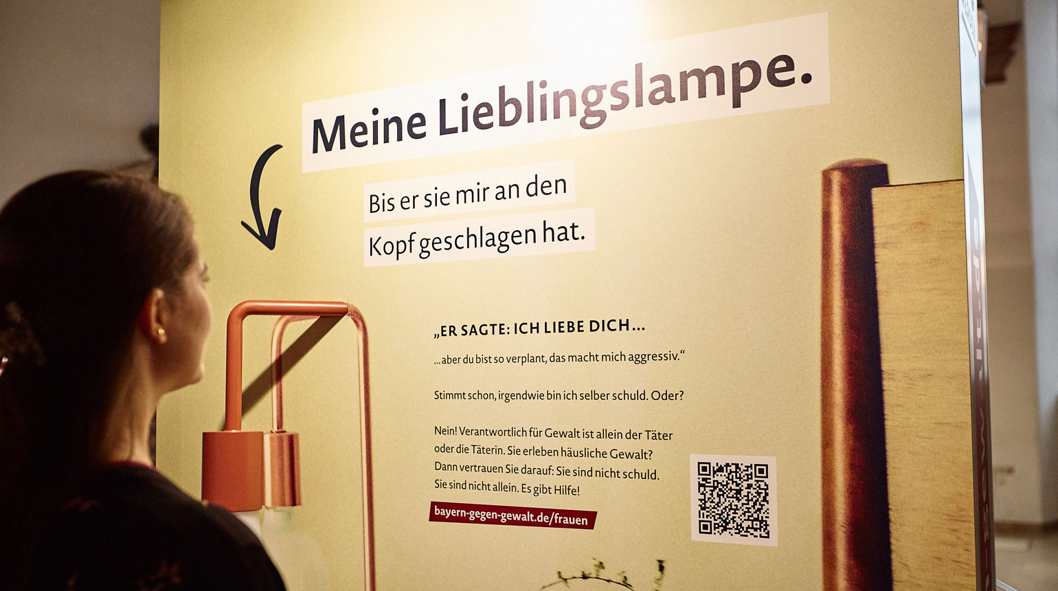 Eine Frau schaut auf ein Ausstellungsmodul der Wanderausstellung „Häusliche Gewalt LOSwerden“.