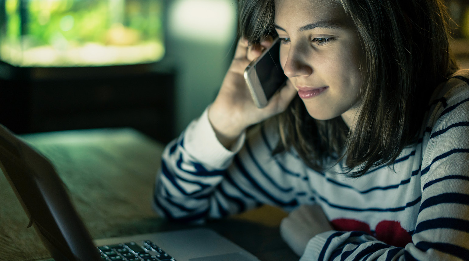 Eine junge Frau sitzt in der Dunkelheit vor einem Computer.  